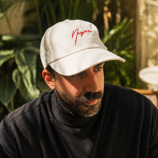 Man wearing a white cap with red text, sitting outdoors with greenery in the background